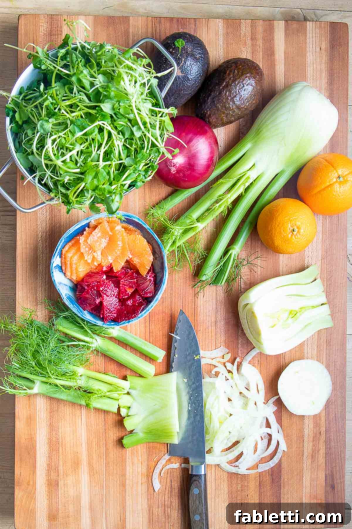 Radiant Orange Fennel 7 Knife cutting fennel into slices. Oranges, watercress avocado and onion in the background.