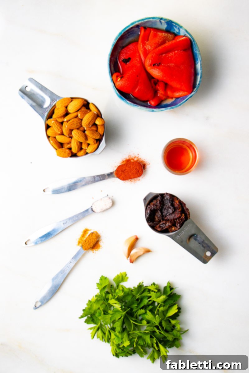 Vibrant Oil-Free Romesco 4 A flat lay of fresh ingredients for Romesco dip including whole almonds, vibrant spices, jarred roasted red peppers, sun-dried tomatoes, fresh garlic cloves, bright parsley, and a bottle of red wine vinegar.