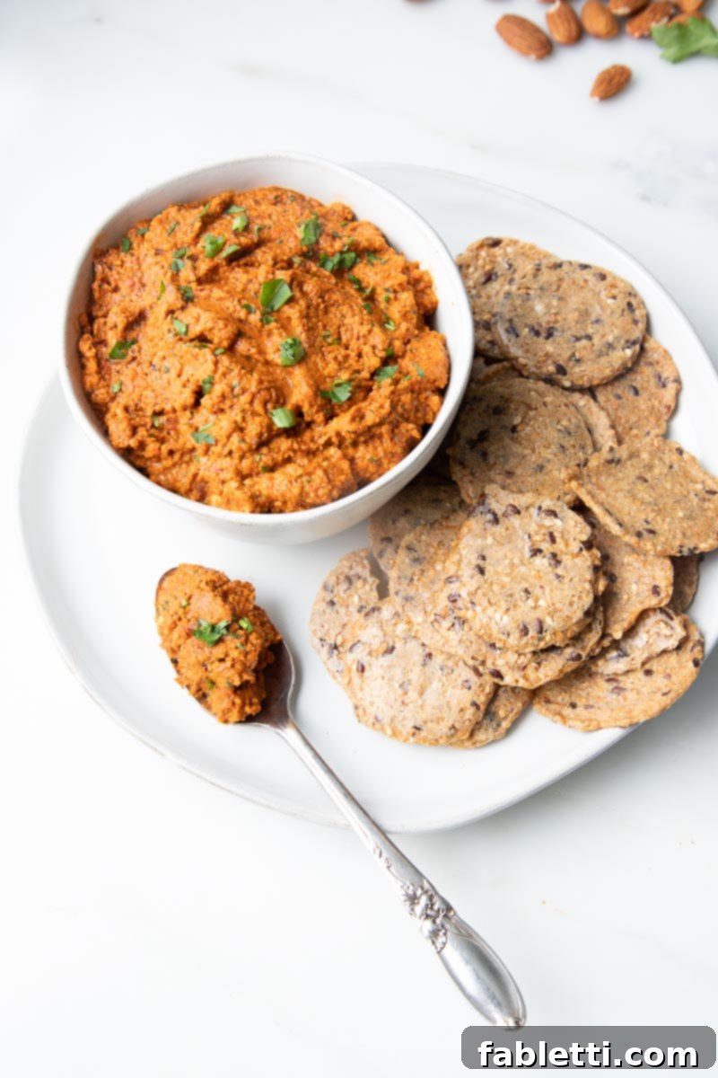 Vibrant Oil-Free Romesco 6 A bowl of vibrant Romesco Dip surrounded by a variety of crispy crackers, ideal for dipping.