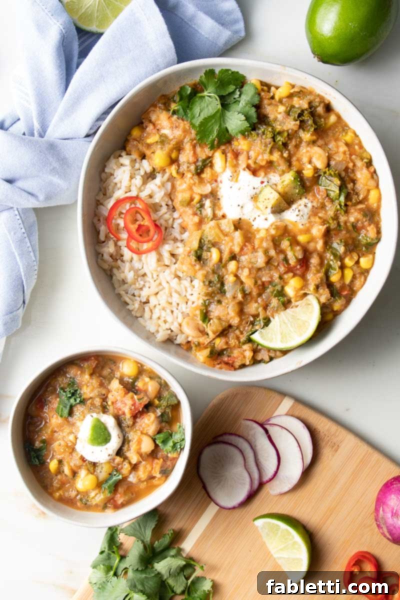 Hearty Vegan White Bean Chili 8 A vibrant serving of white bean chili with rice, fresh greens, lime wedges, and other colorful vegetables.