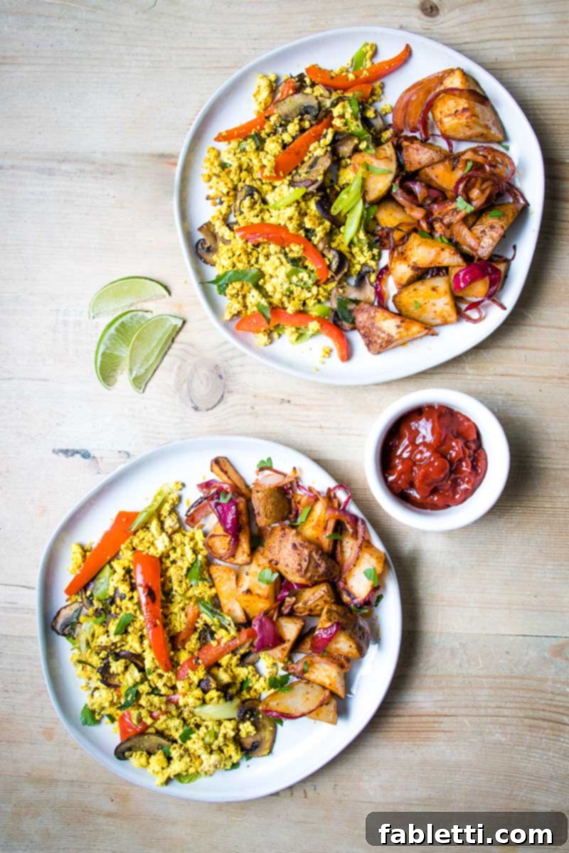 Golden Tofu Scramble 2 Two white plates on a wood table loaded with colorful veggie scramble and potatoes plus a dish of ketchup