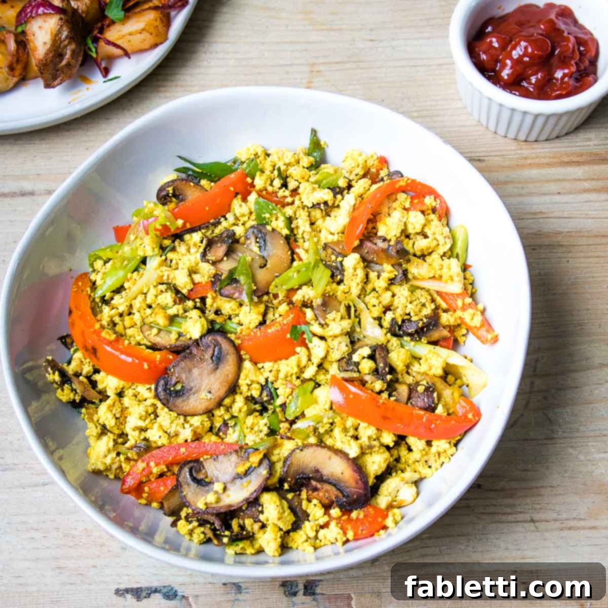 Golden Tofu Scramble 3 Large bowl filled with tofu scramble, mushrooms, peppers, scallions and a side dish of ketchup