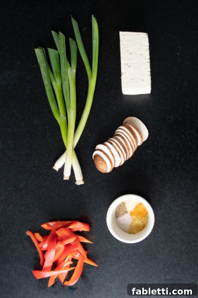 Golden Tofu Scramble 4 Various scramble ingredients laid out on a cutting board, including tofu, mushrooms, red bell peppers, scallions, and spices.