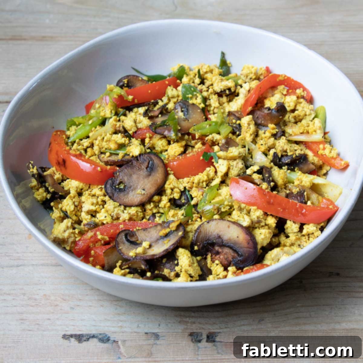 Golden Tofu Scramble 9 Sauteed mushrooms, peppers, scallions in a large white bowl with scrambled tofu.