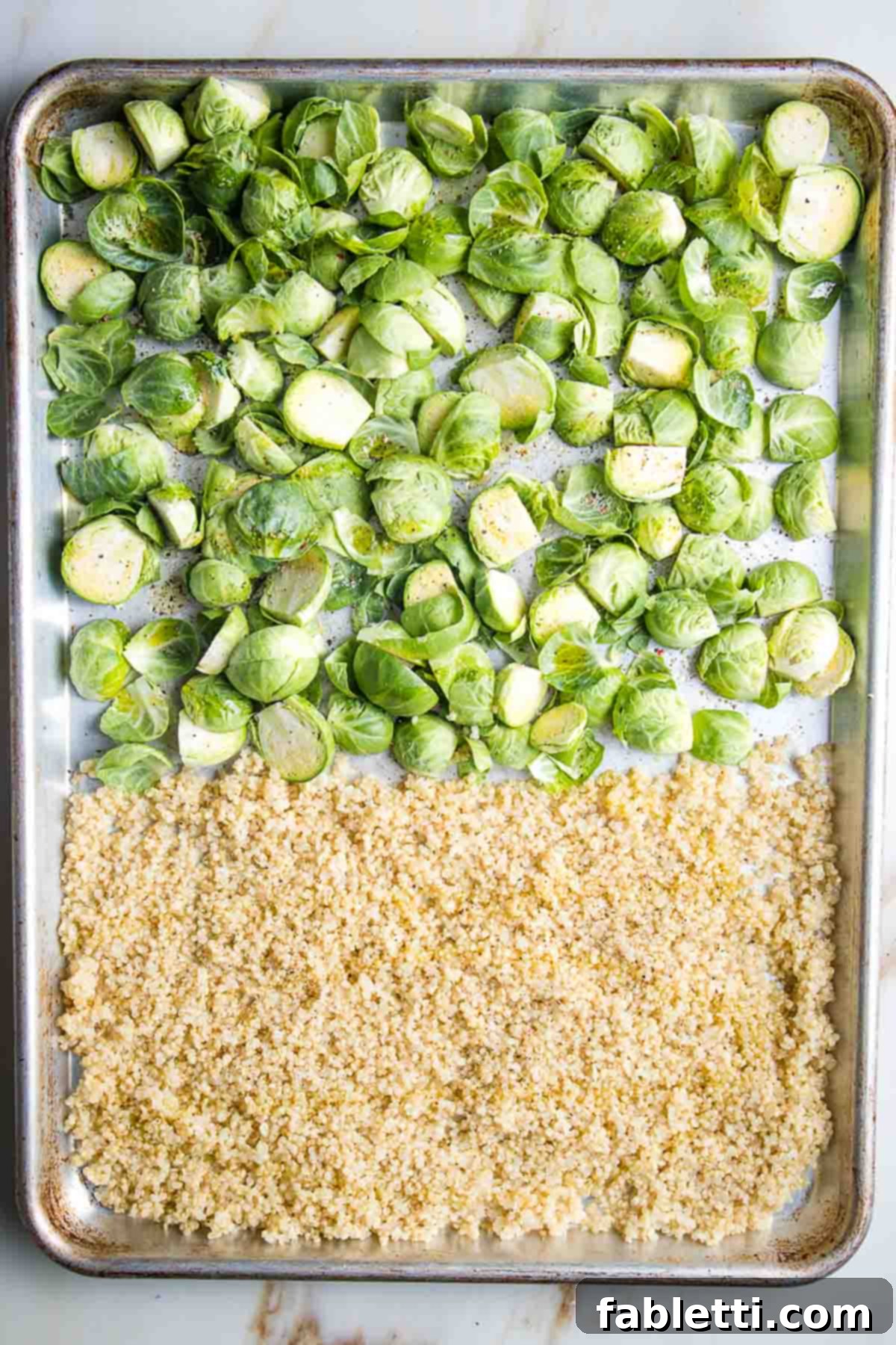 Golden Crisp Quinoa Salad with Silky Plant-Based Dressing 4 A large baking tray, half filled with cooked quinoa spread thinly and the other half with trimmed Brussels sprouts, ready for roasting.