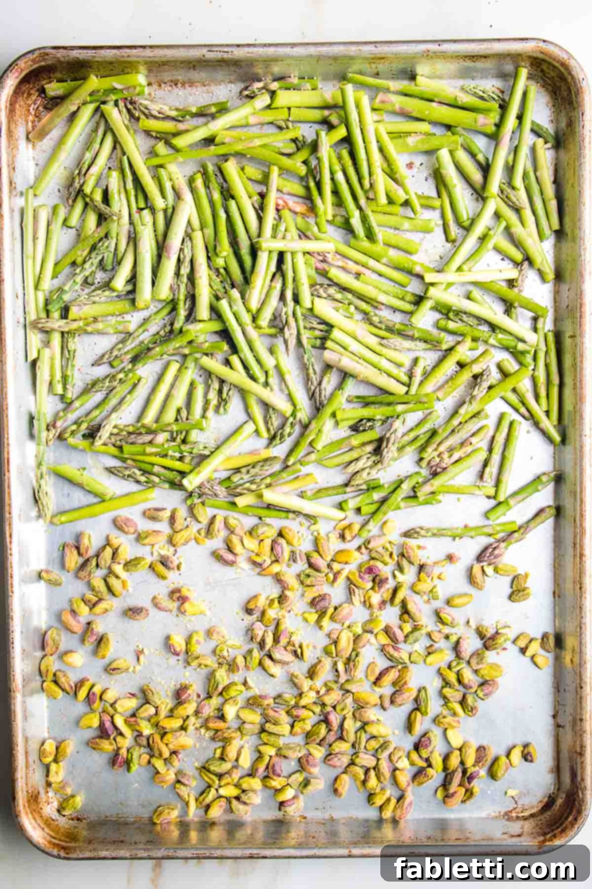 Golden Crisp Quinoa Salad with Silky Plant-Based Dressing 5 Another large baking tray with asparagus pieces laid out on one side and raw pistachios on the other, ready for roasting.