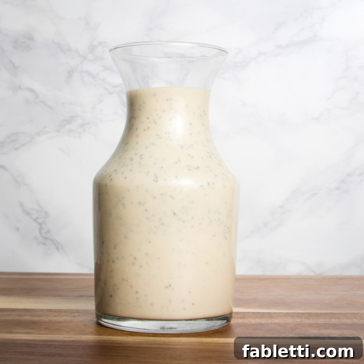 Golden Crisp Quinoa Salad with Silky Plant-Based Dressing 8 A glass pitcher filled with a creamy, pale yellow salad dressing.