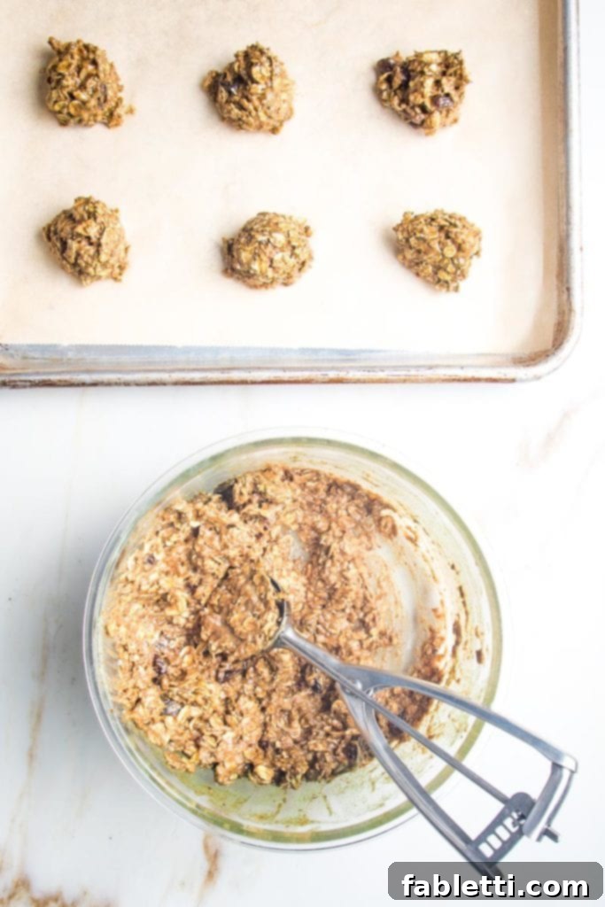 Speedy 15-Minute Oatmeal Raisin Delights 6 A small ice cream scoop neatly portions out oatmeal cookie dough onto a baking tray lined with parchment paper, ready for baking.