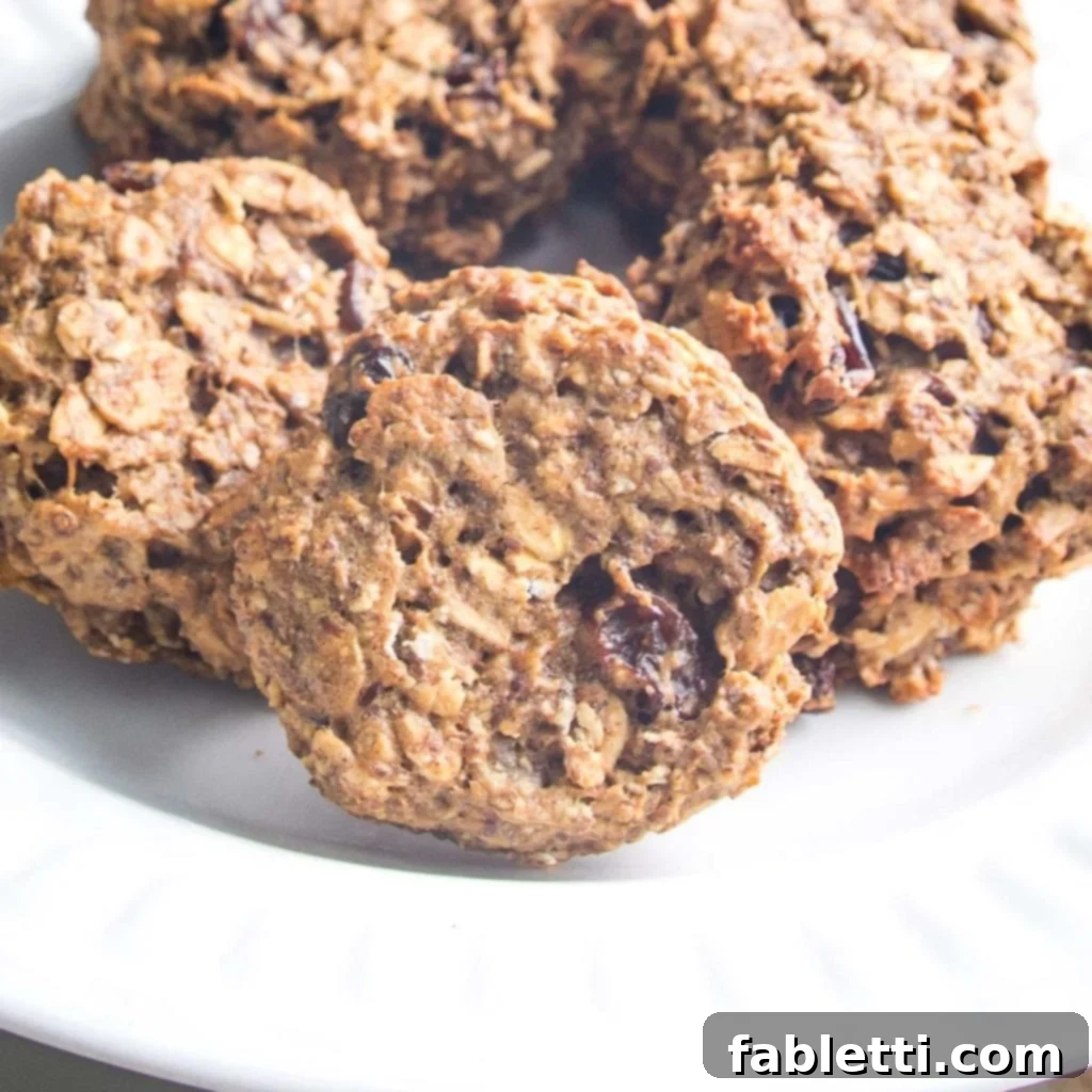 Speedy 15-Minute Oatmeal Raisin Delights 9 A close-up of a single oatmeal raisin cookie placed on a white plate, with more cookies blurred in the background, emphasizing its wholesome texture.