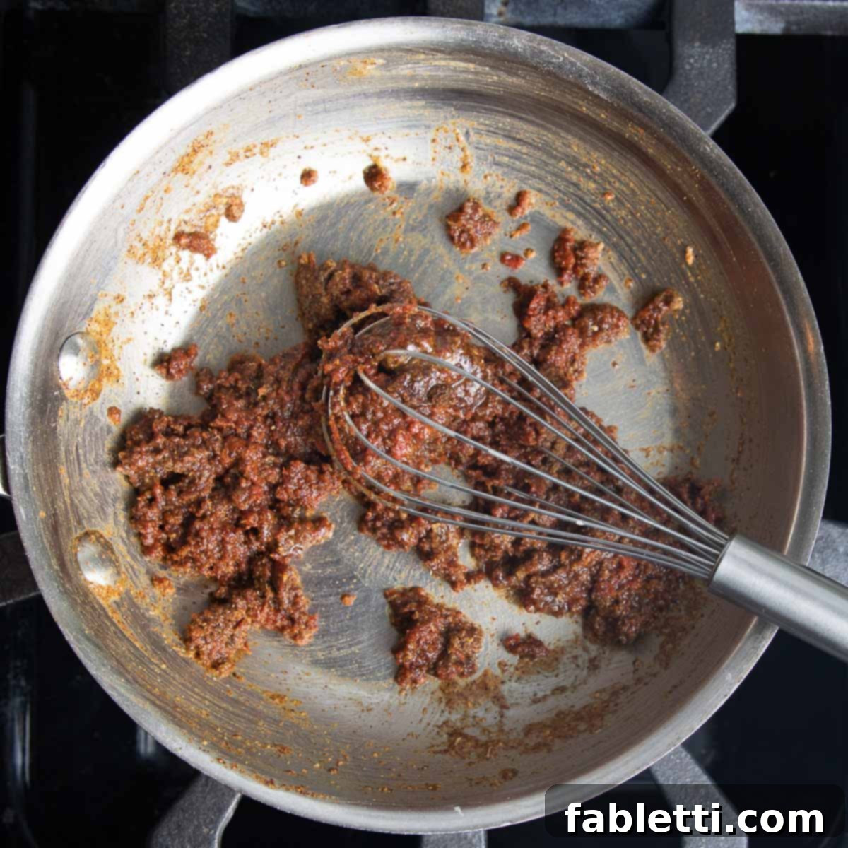 Making enchilada sauce by whisking together tomato paste, spices and roux to form a paste.