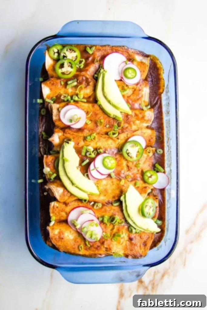 Hearty Plant-Based Enchilada Bake 2 Enchilada Casserole: Baking Dish filled with tortillas that are stuffed with veggies and topped with enchilada sauce and colorful toppings.