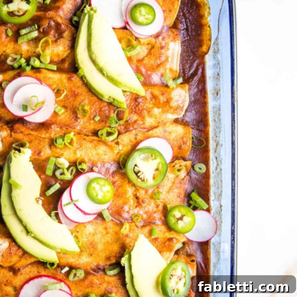 Hearty Plant-Based Enchilada Bake 11 Casserole Dish with enchiladas, garnished with avocado slices, jalapenos and radishes.