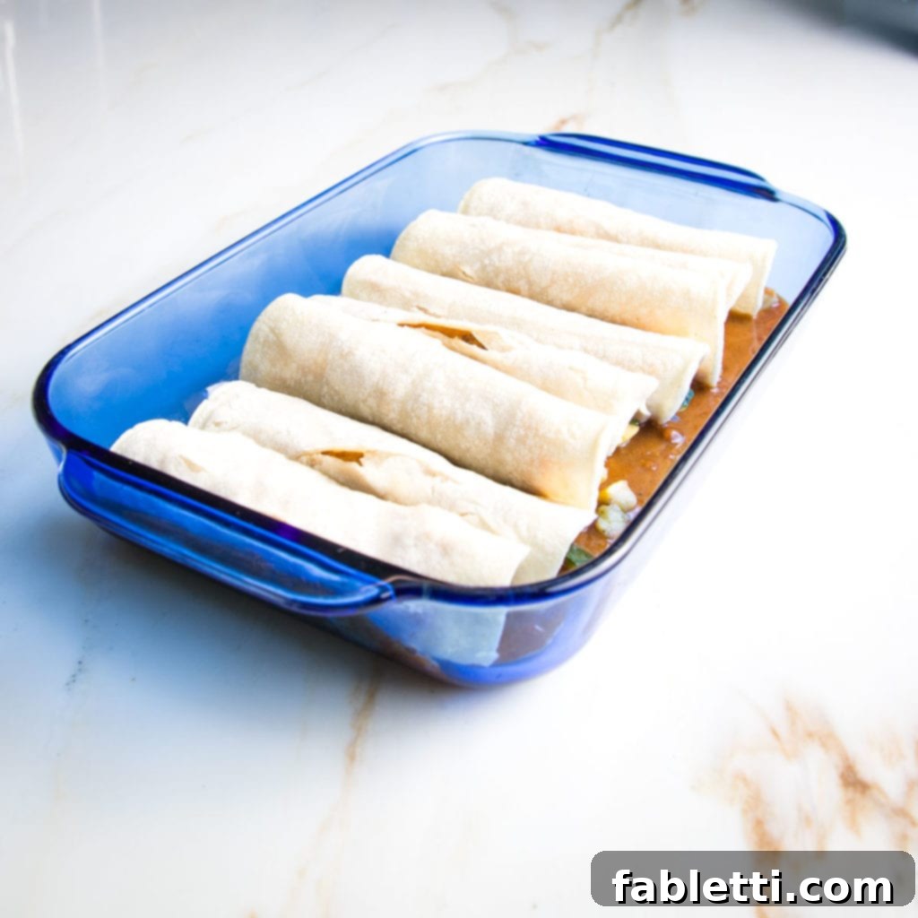 Hearty Plant-Based Enchilada Bake 8 Blue glass casserole dish loaded with enchiladas on top of red sauce.