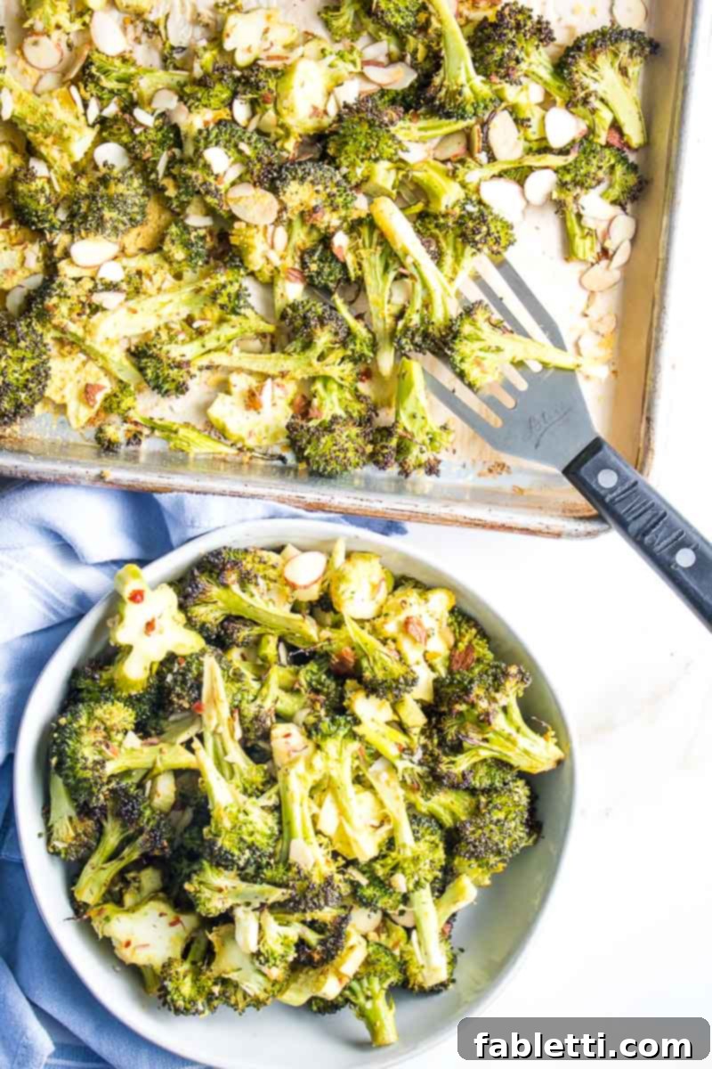 Sheet Pan of roasted broccoli with a spatula loading it into a bowl. Golden brown crispy broccoli florets and stems, with a hint of lemon and almonds. 