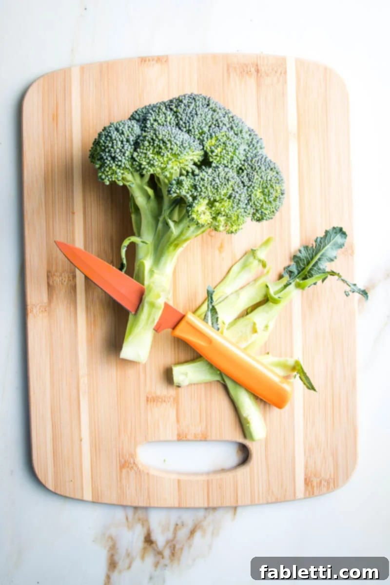 Paring knife cutting off the woody outer layer of a head of broccoli stem.