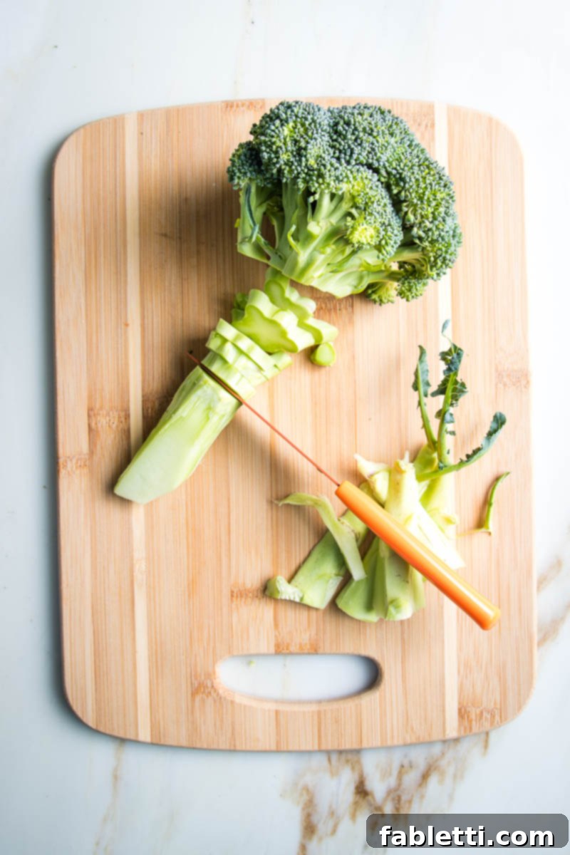 Slicing the stem of a head of broccoli into ¼" discs, showing the uniform pieces.