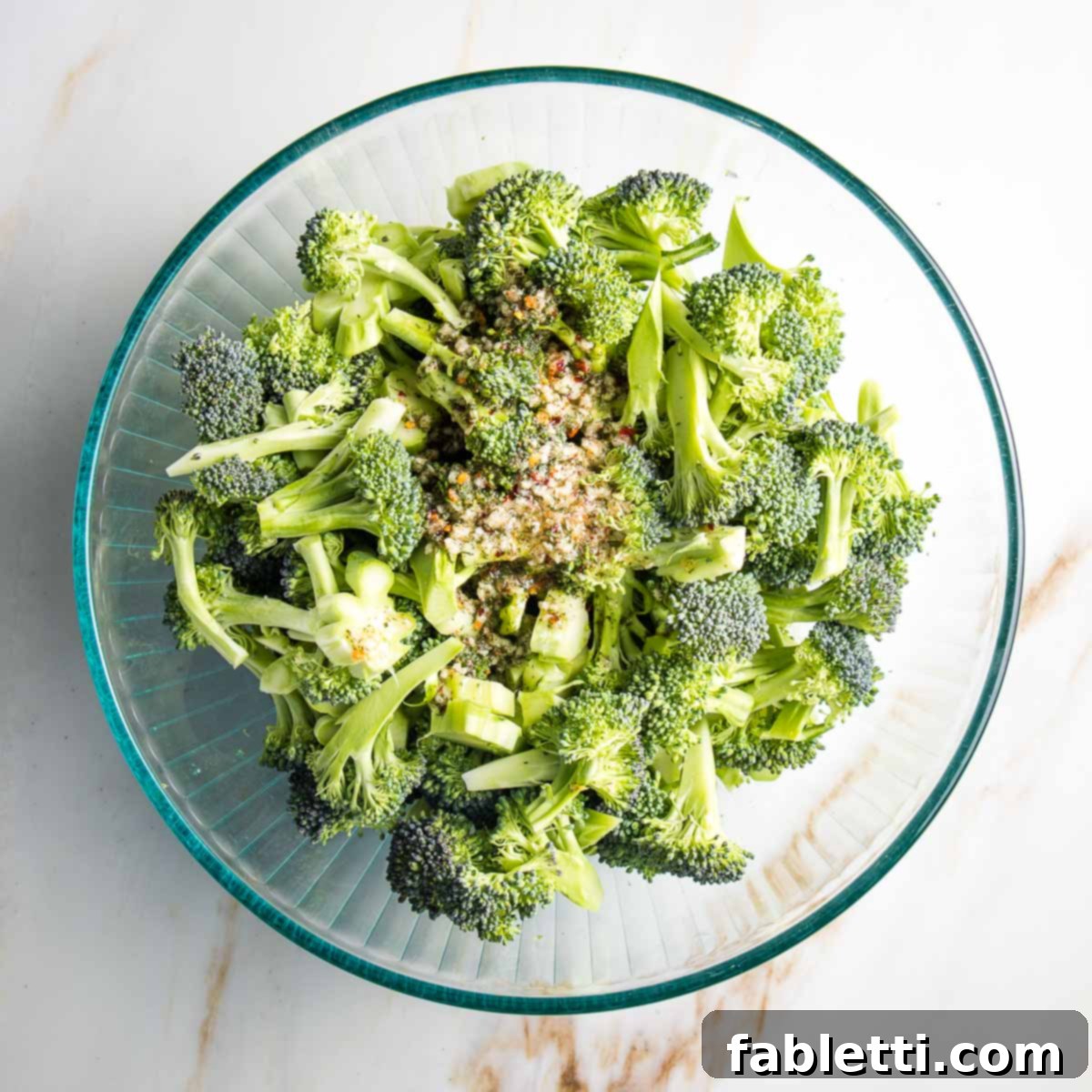 Large bowl of trimmed broccoli coated evenly with the vibrant marinade, ready for roasting.