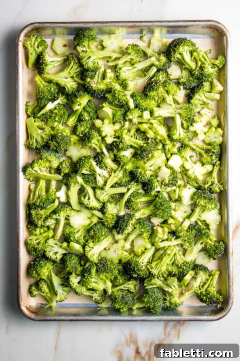 Marinated broccoli florets and stems spread in a single layer on a parchment-lined baking sheet.