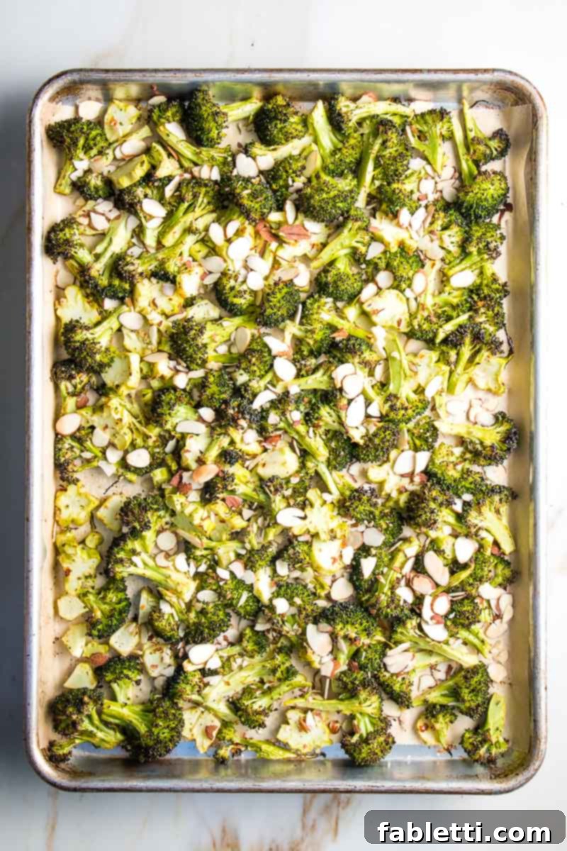 Roasted broccoli on a sheet pan, with sliced almonds sprinkled over and ready for the final roast.