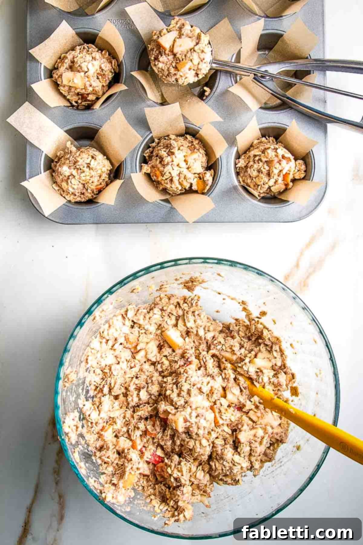 Using a small scoop to distribute muffin batter into prepared muffin tins lined with parchment paper.