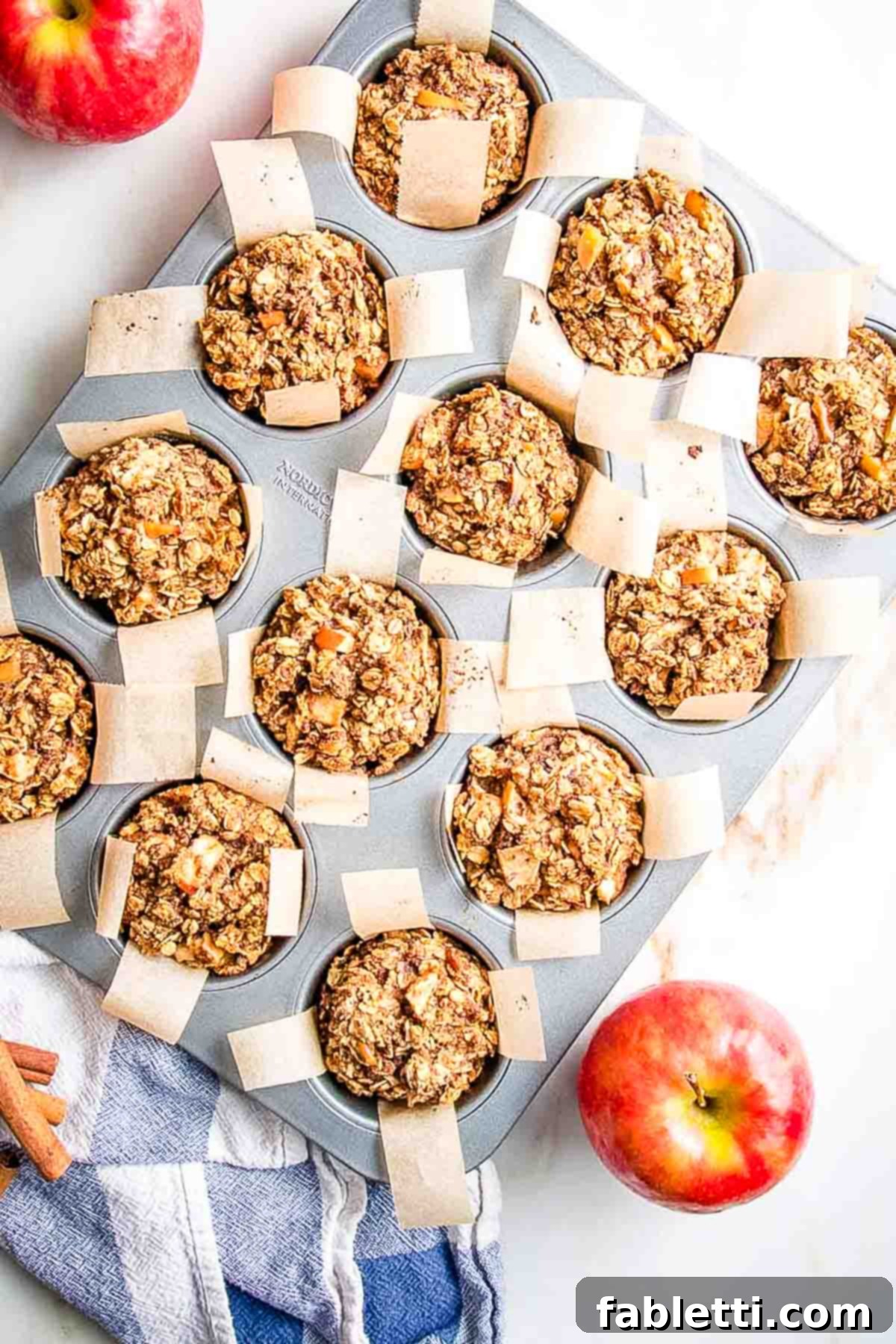 Chunks of apples visible in oatmeal muffins perfectly lined with parchment paper in muffin tins.
