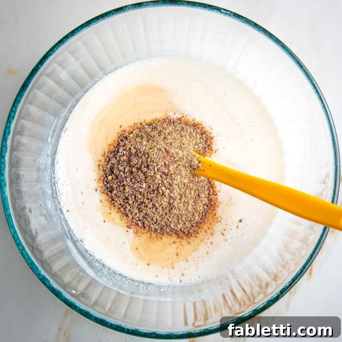 Ground flaxseed being stirred into the wet ingredient mixture for vegan apple oatmeal muffins.