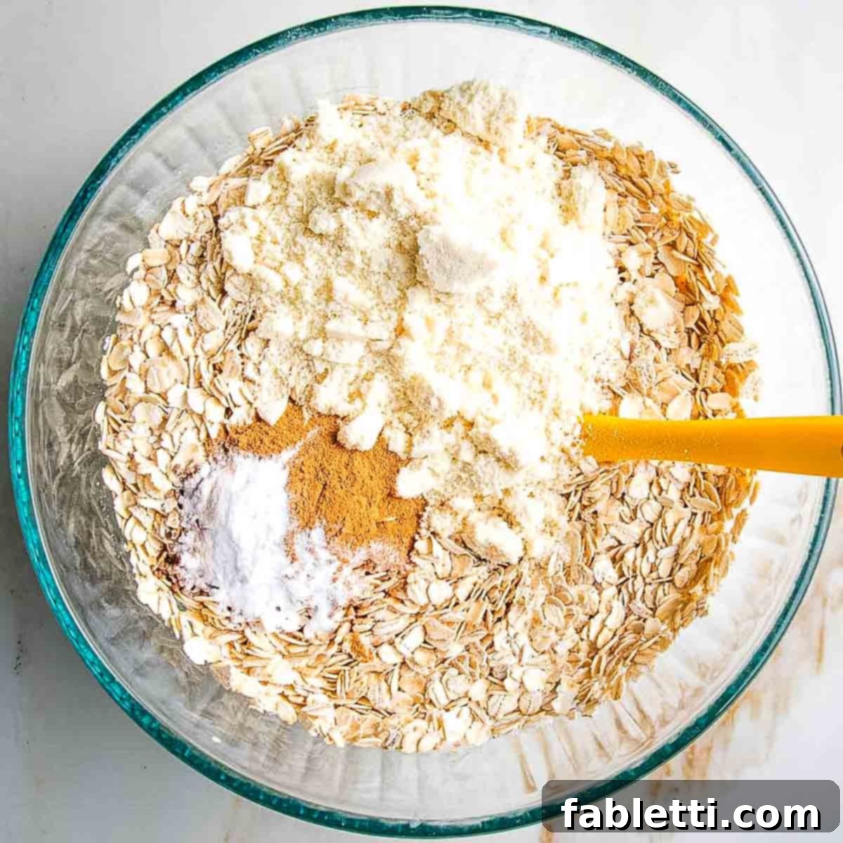 Dry ingredients, including oats, almond flour, arrowroot powder, baking powder, cinnamon, allspice, ginger, nutmeg, and sea salt, being sprinkled over the wet mixture.