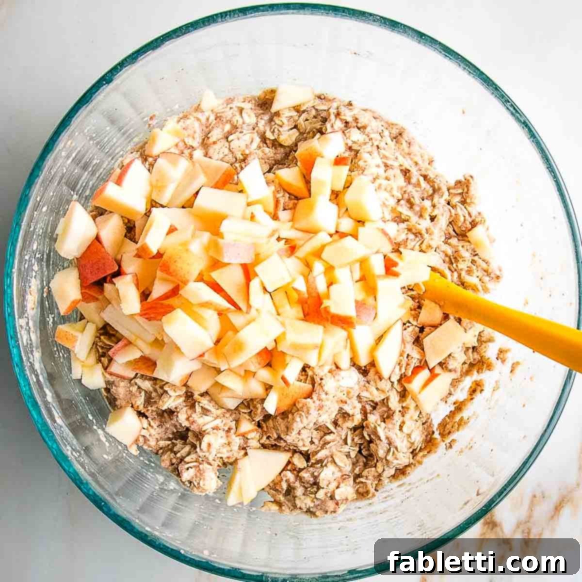 Diced apples being stirred into the vegan oatmeal muffin batter.
