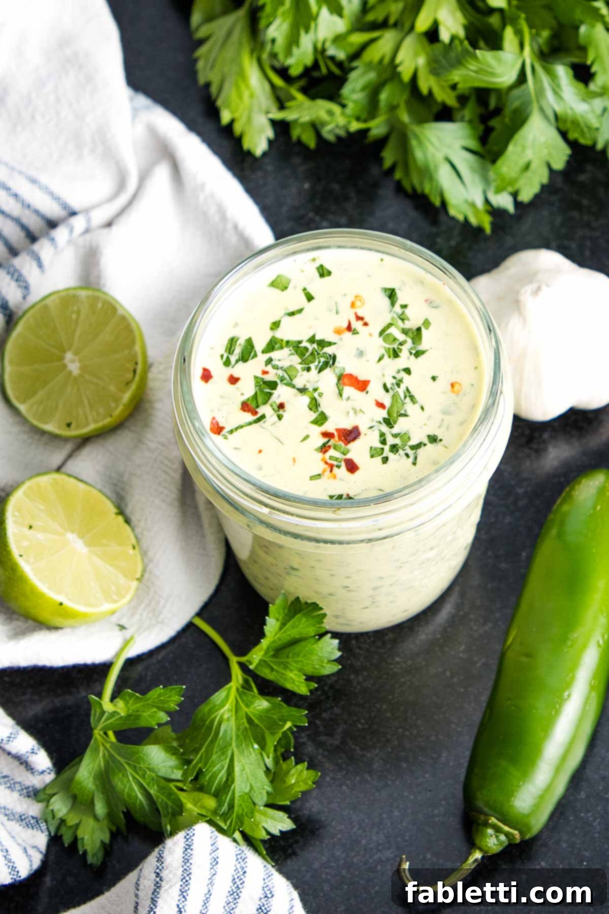Vibrant green tahini sauce elegantly presented in a clear mason jar, adorned with delicate specks of fresh herbs and a hint of crushed red pepper, ready to tantalize taste buds.