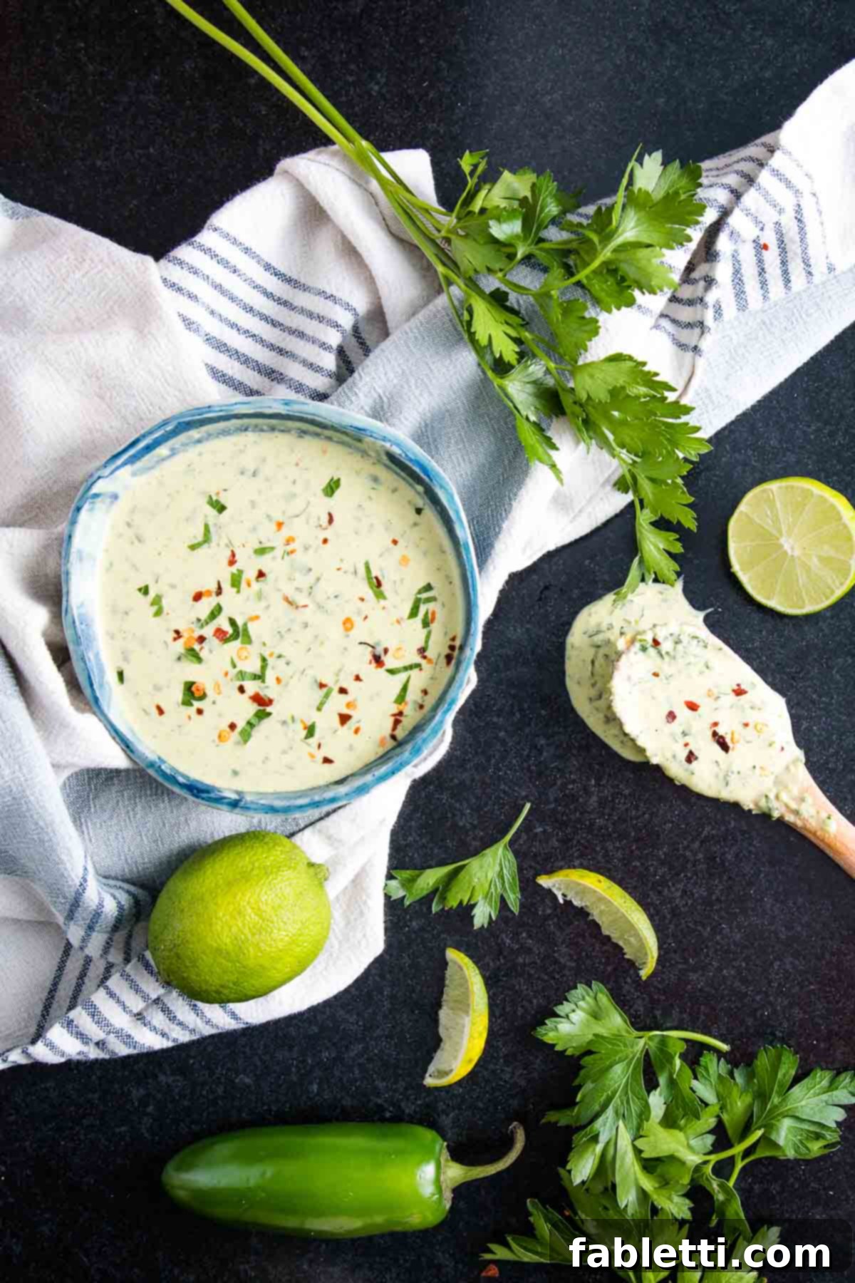 A beautifully presented bowl of creamy green tahini sauce, surrounded by fresh, vibrant ingredients like whole limes, fragrant fresh parsley, and bright green jalapenos, highlighting its natural goodness.