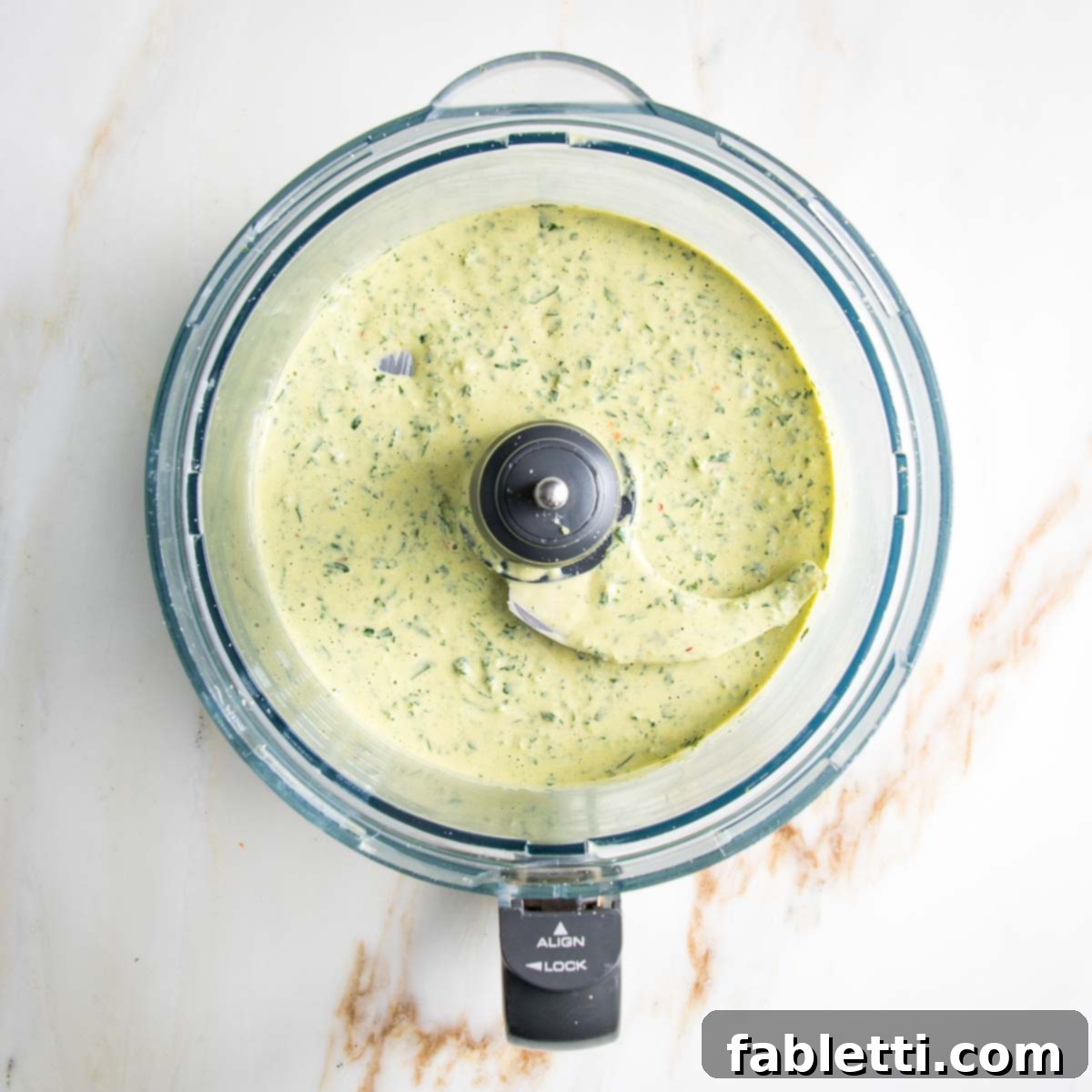 The food processor bowl contains a freshly blended, creamy green sauce, indicating it is now perfectly smooth and ready for serving, showcasing its vibrant color and luxurious texture.
