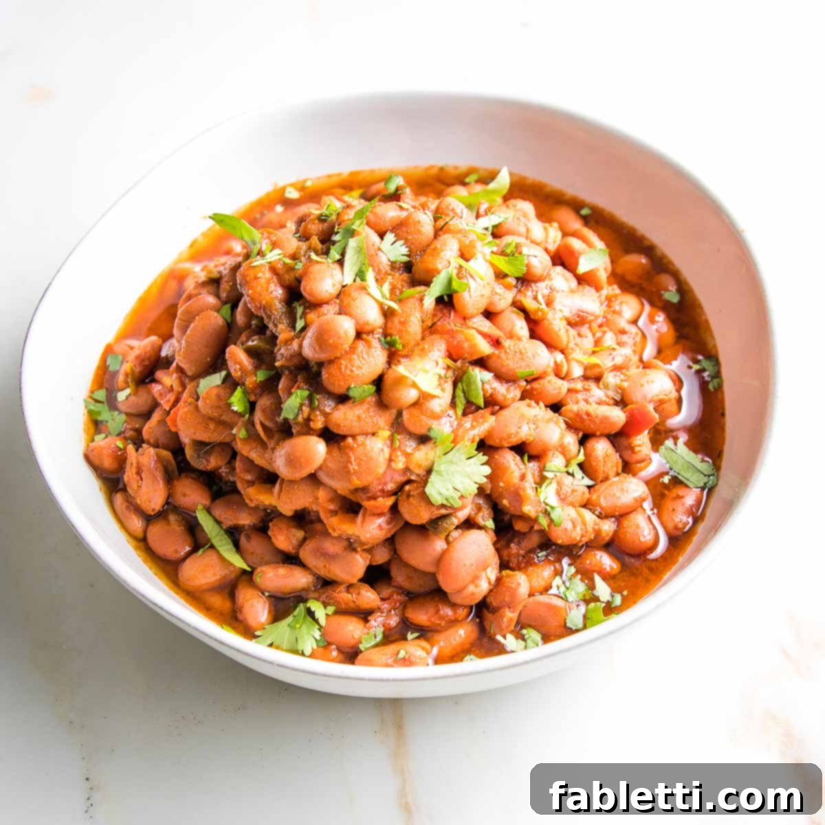 Easy Instant Pot Mexican Pinto Beans 2 Mexican style beans with fresh herbs in a white bowl.