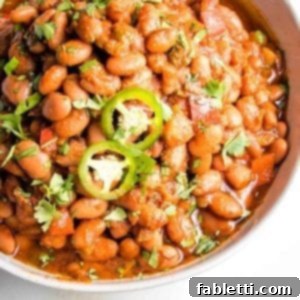 Easy Instant Pot Mexican Pinto Beans 13 Close up of a white bowl of pinto beans in a tomato based sauce, topped with jalapeno slices and sprinkled with cilantro