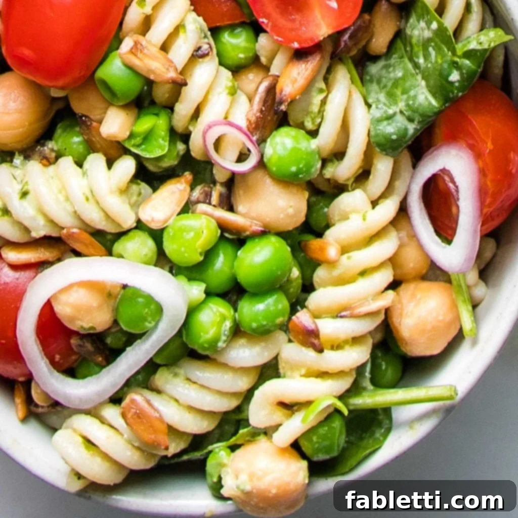 No-Fuss Summer Pasta Salad 6 A close-up shot of corkscrew pasta tossed with thinly sliced shallot rings, bright green peas, plump chickpeas, halved cherry tomatoes, fresh spinach, and crunchy sunflower seeds.