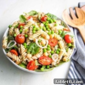 No-Fuss Summer Pasta Salad 7 Large white bowl filled with cherry tomatoes, fusilli pasta, green peas, chickpeas, sunflower seeds with a striped blue napkin on the side.
