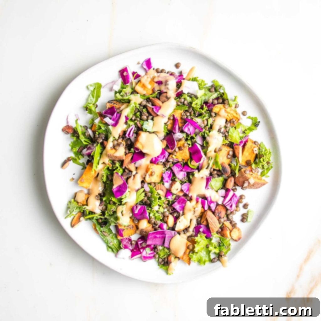 Vibrant Vegan Lentil Medley 2 A beautifully arranged vegan lentil salad on a white round plate, showcasing colorful vegetables and diagonal stripes of creamy dressing.