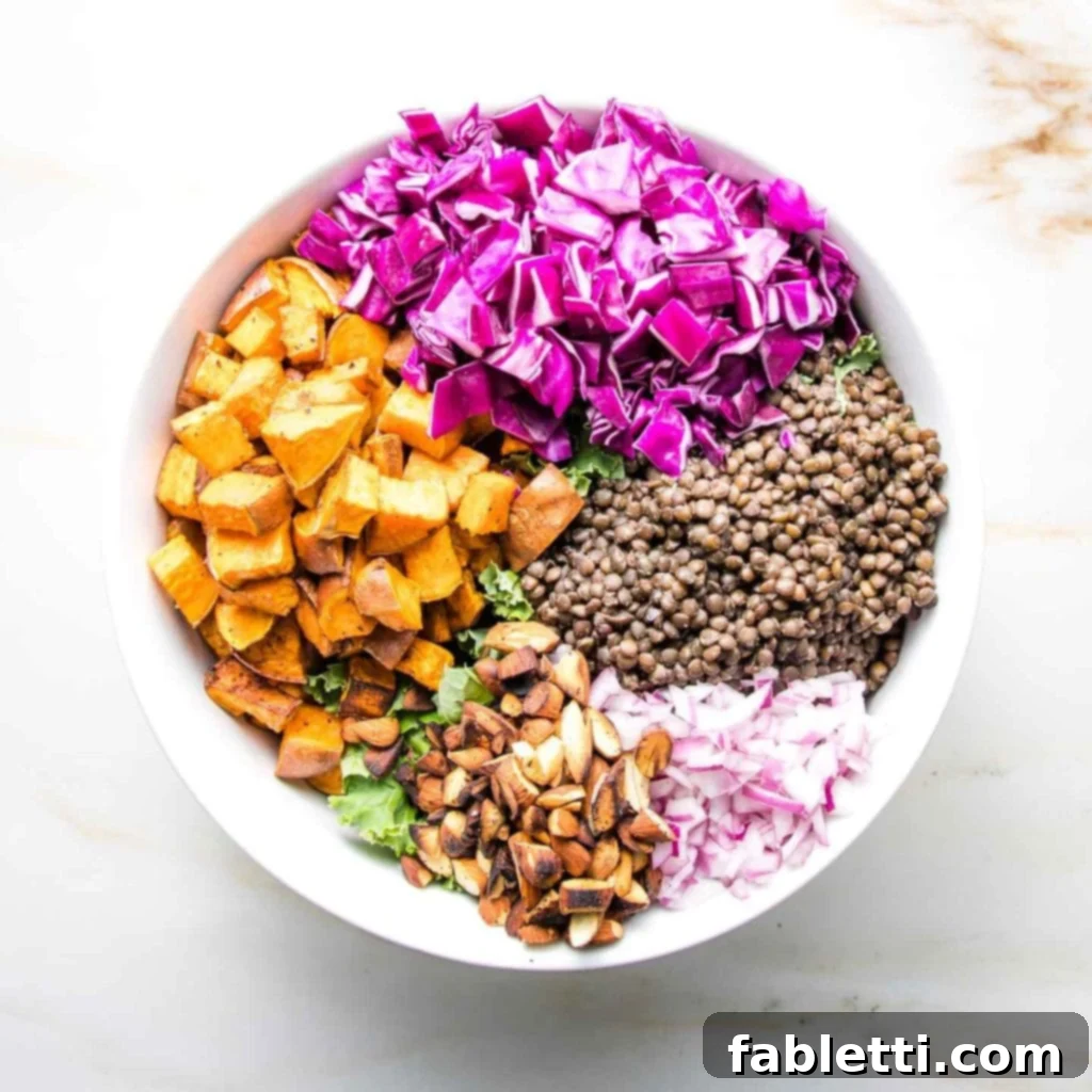 Vibrant Vegan Lentil Medley 11 A white bowl showcasing cubes of sweet potatoes, coarsely chopped purple cabbage, cooked black lentils, chopped red onion, and toasted almonds.