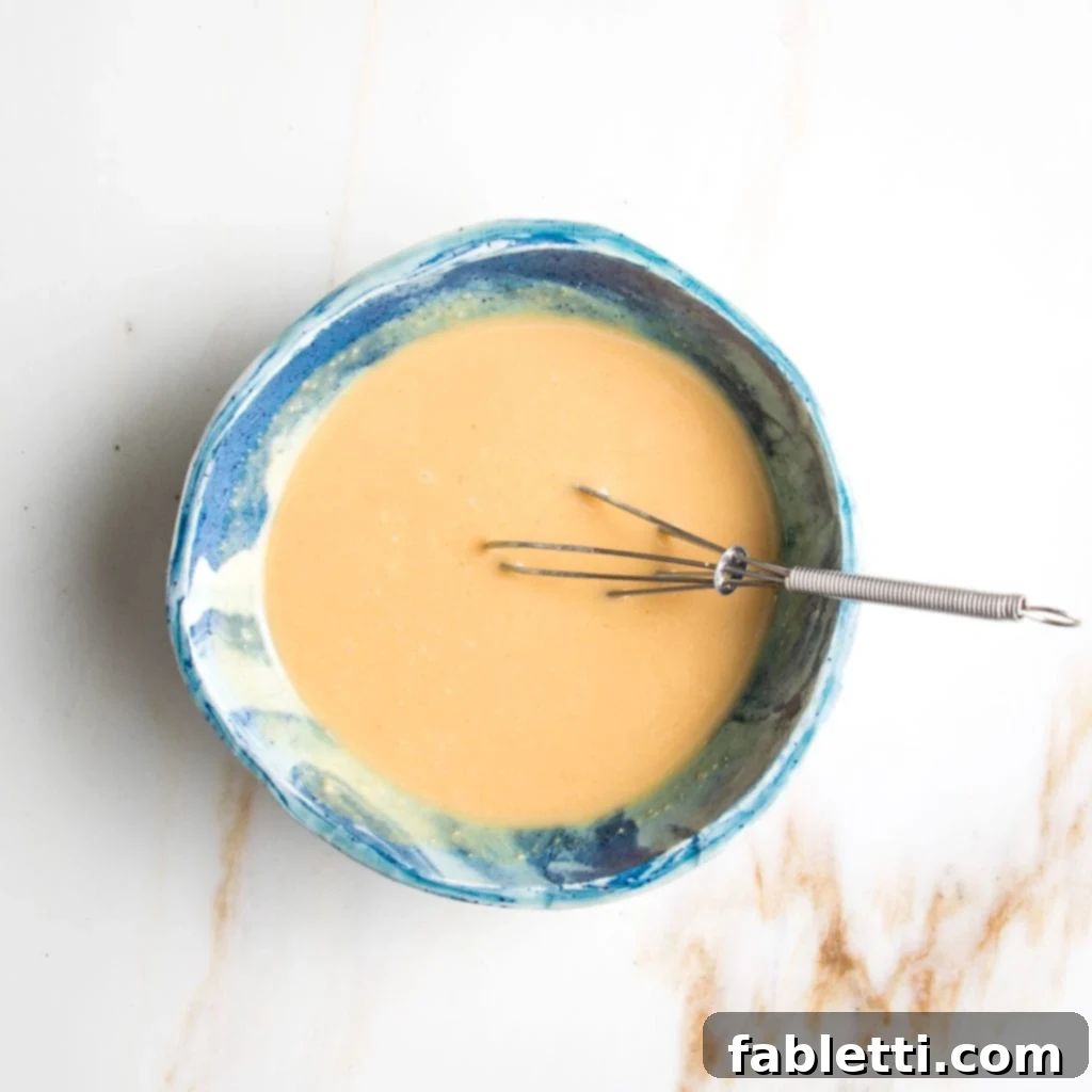 Vibrant Vegan Lentil Medley 5 Simple miso mustard dressing in a bright blue bowl with a whisk.