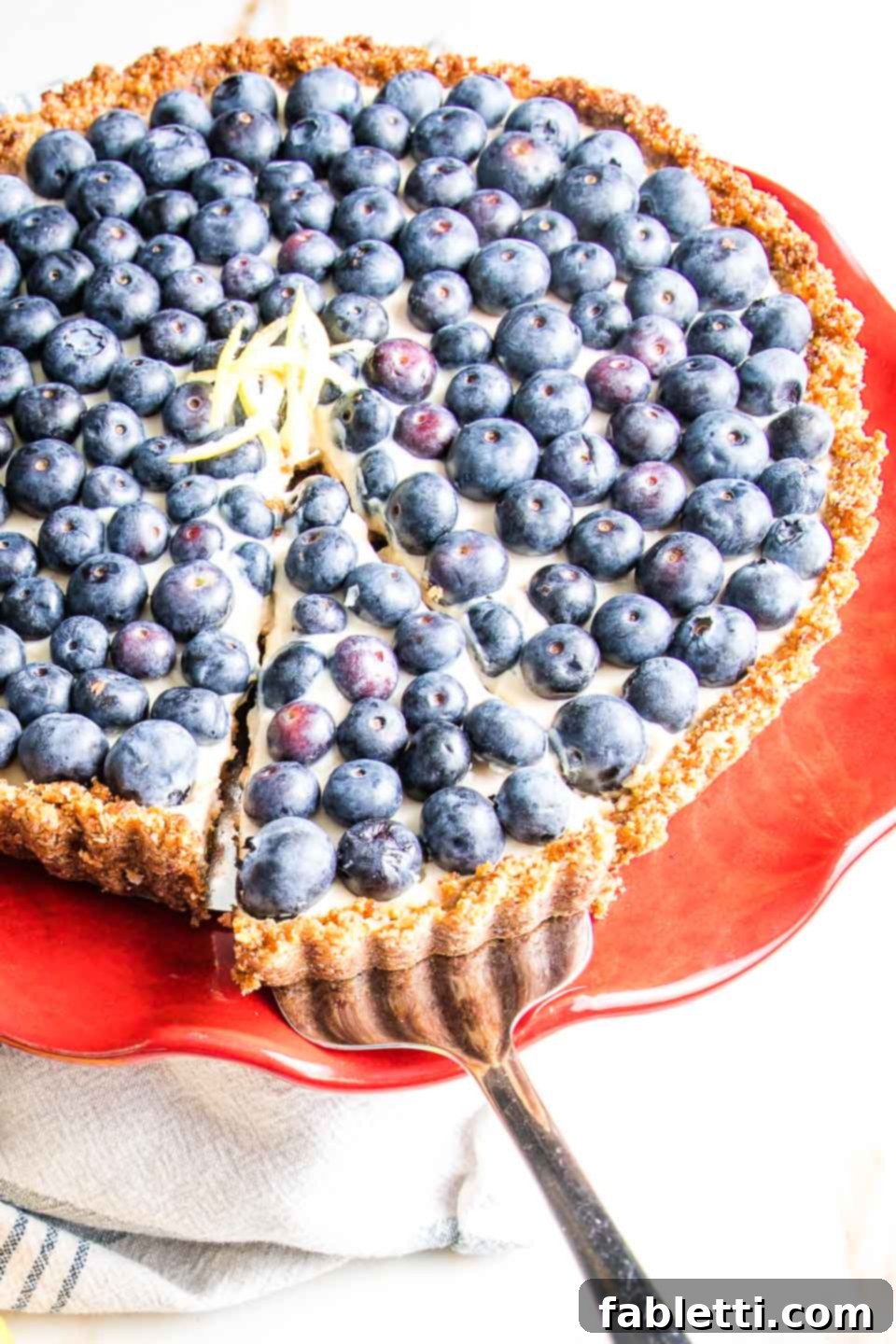 Homemade Blueberry Tart Perfection 10 A hand gently pulling out a slice of the homemade blueberry tart from a bright red cake stand, showcasing its inviting appearance.