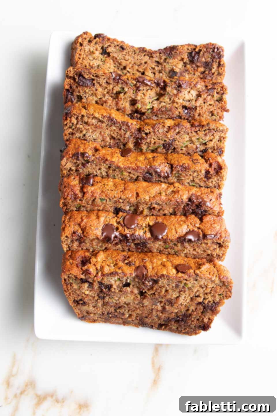 Wholesome Vegan Zucchini Bread Sweetened with Applesauce 2 Slices of healthy chocolate chip zucchini bread arranged beautifully on a white platter, showcasing its moist texture and delicious chocolate chunks.