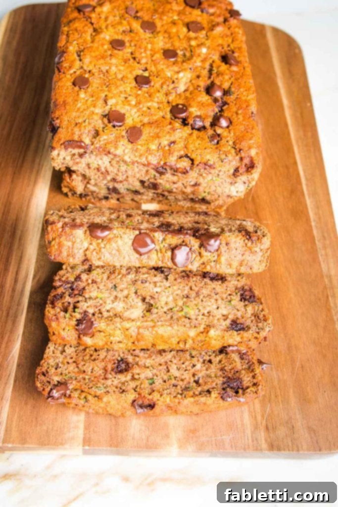 Wholesome Vegan Zucchini Bread Sweetened with Applesauce 11 Irresistibly moist and healthy chocolate chip zucchini bread slices neatly arranged on a rustic wood-grained cutting board, highlighting its delightful texture.