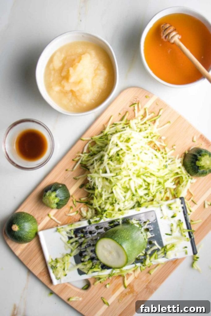 Wholesome Vegan Zucchini Bread Sweetened with Applesauce 4 A collection of fresh zucchini bread ingredients including honey, applesauce, vanilla extract, and freshly shredded, unpeeled zucchini.