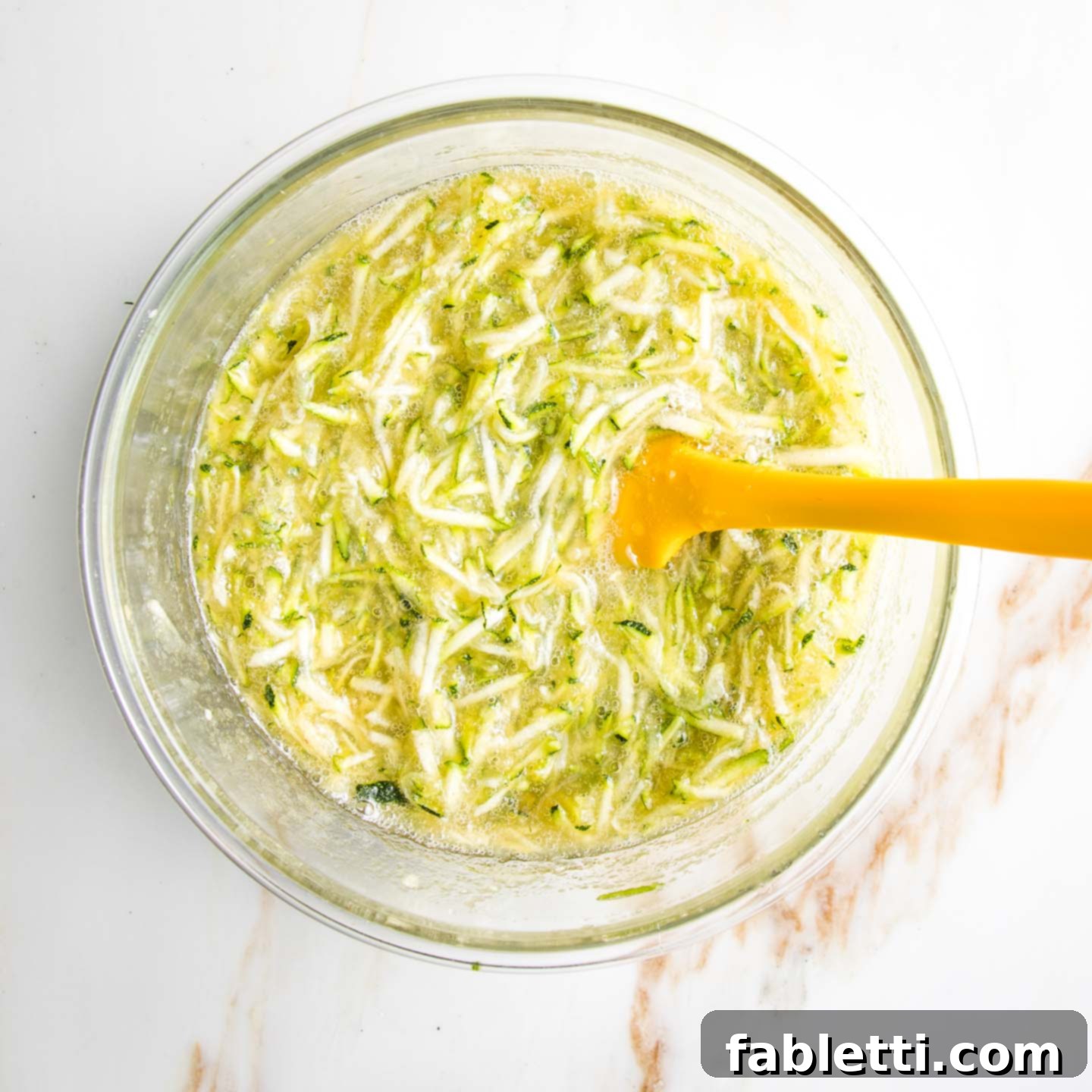 Wholesome Vegan Zucchini Bread Sweetened with Applesauce 5 Freshly shredded zucchini mixed with sweet applesauce and golden honey in a bowl, ready for the next step.