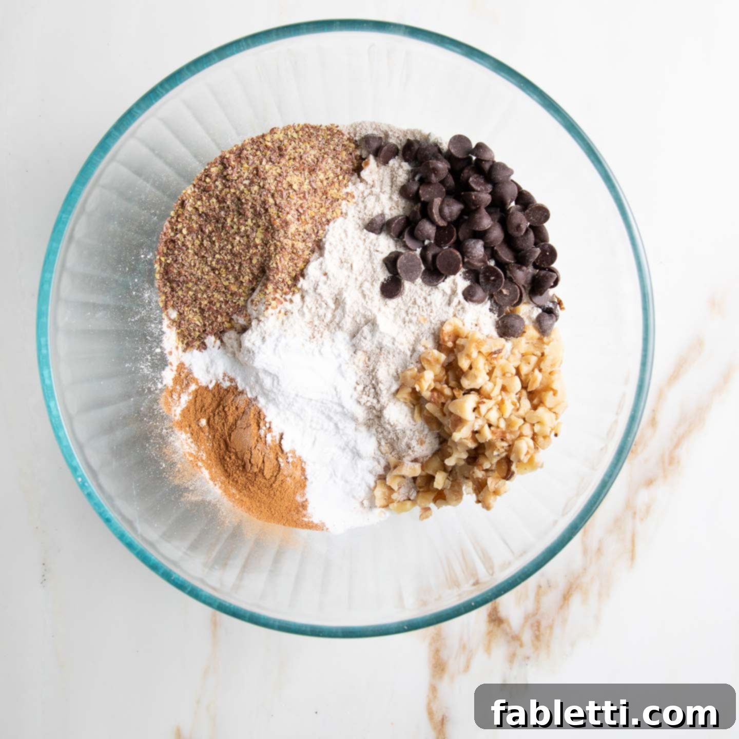 Wholesome Vegan Zucchini Bread Sweetened with Applesauce 6 A bowl filled with dry ingredients: whole grain flour, ground flax, aromatic cinnamon, baking powder, baking soda, and salt, along with optional chocolate chips and chopped walnuts.