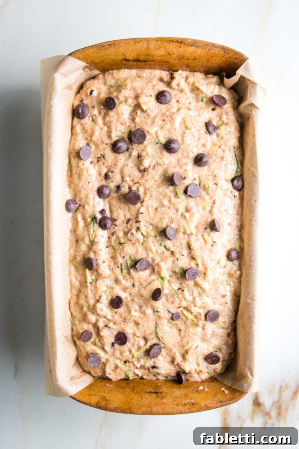 Wholesome Vegan Zucchini Bread Sweetened with Applesauce 8 A loaf of healthy chocolate chip zucchini bread, perfectly portioned in its parchment-lined pan, ready for baking in the oven.