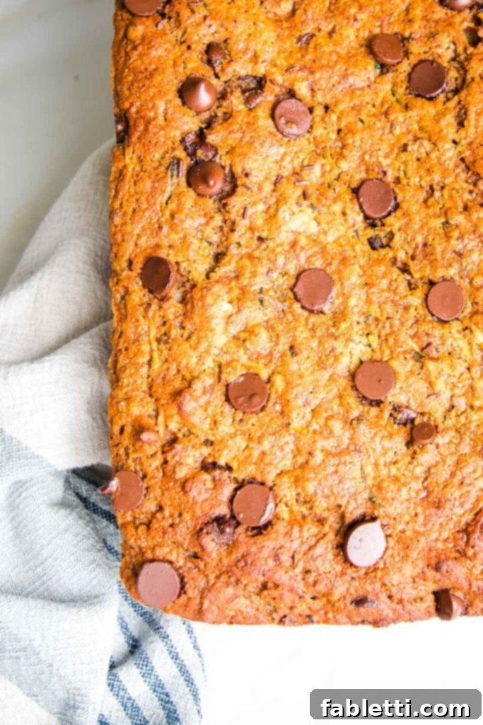 Wholesome Vegan Zucchini Bread Sweetened with Applesauce 10 A warm, golden loaf of healthy and moist zucchini bread with visible chocolate chips, cooling gracefully on a cotton tea towel.