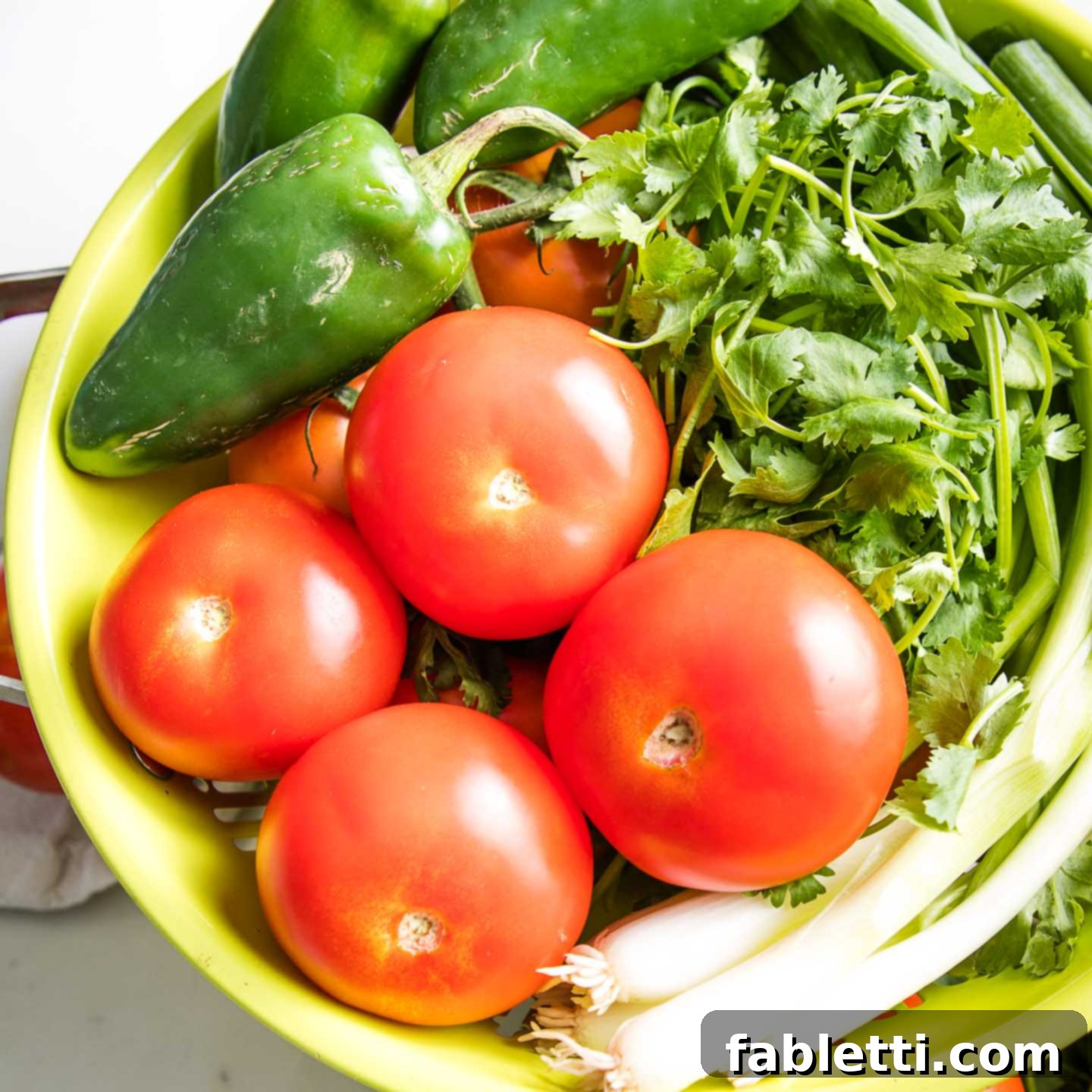 Vibrant Chunky Tomato Salsa 3 A light green colander filled with fresh tomatoes, jalapenos, scallions and cilantro.