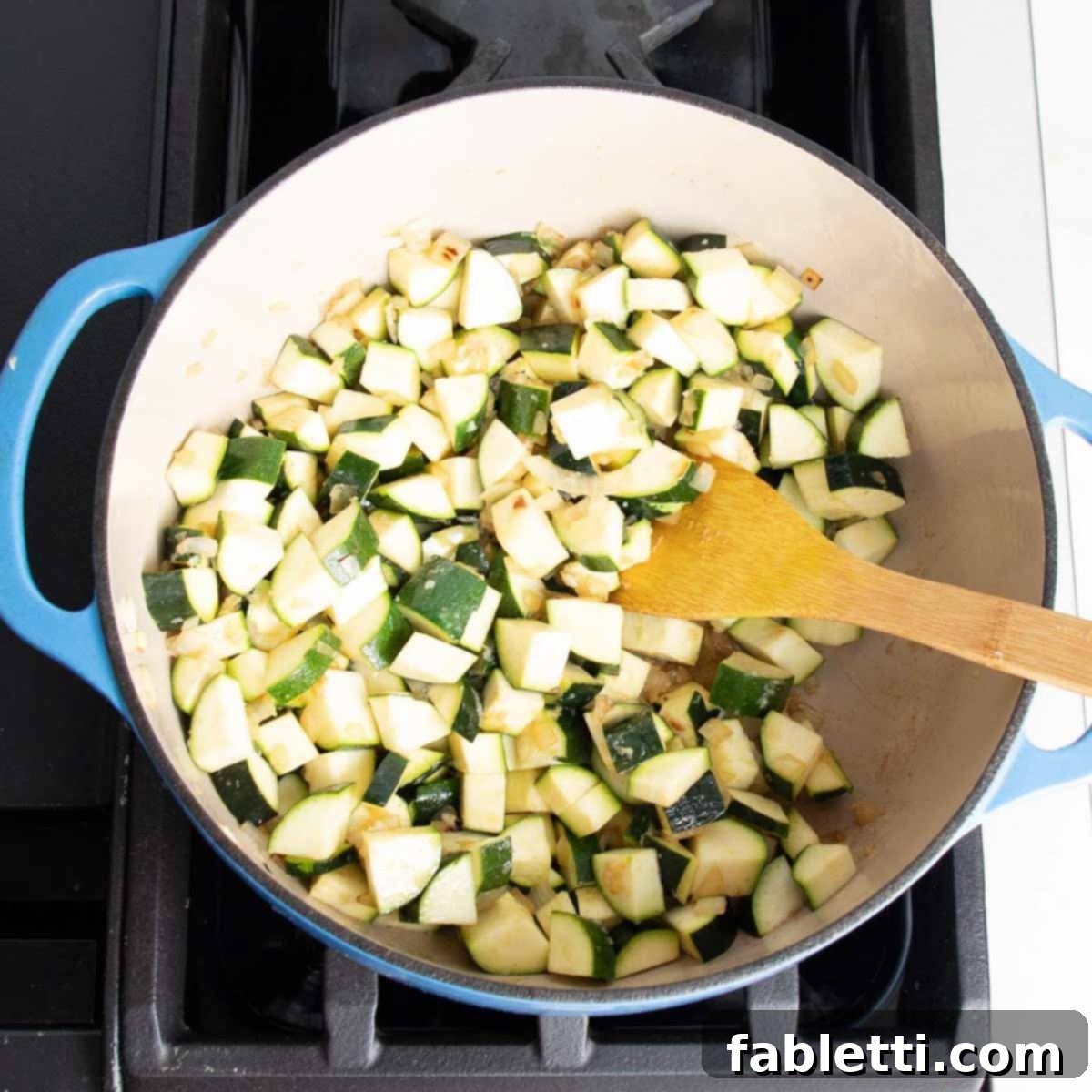 Velvety Zucchini Soup 7 Dutch oven with chopped zucchini, onions, garlic and a wooden spoon stirring.