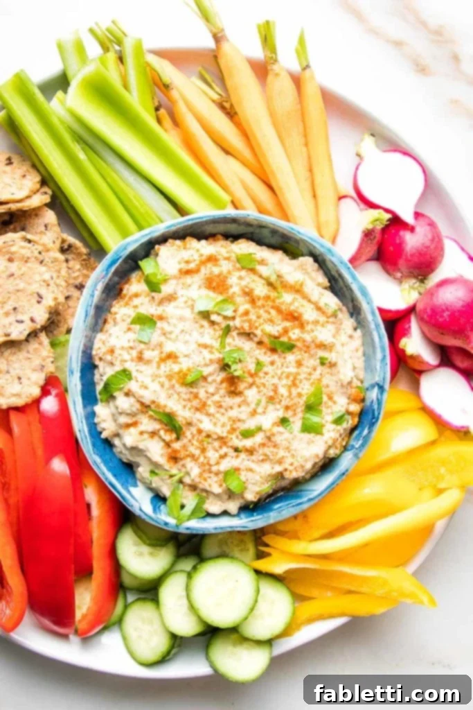 Velvety Roasted Garlic and Tahini Baba Ganoush 2 Baba Ganoush in a blue bowl sprinkled with paprika and fresh parsley with crudites of brightly colored radish, bell peppers, celery, carrots and crackers.