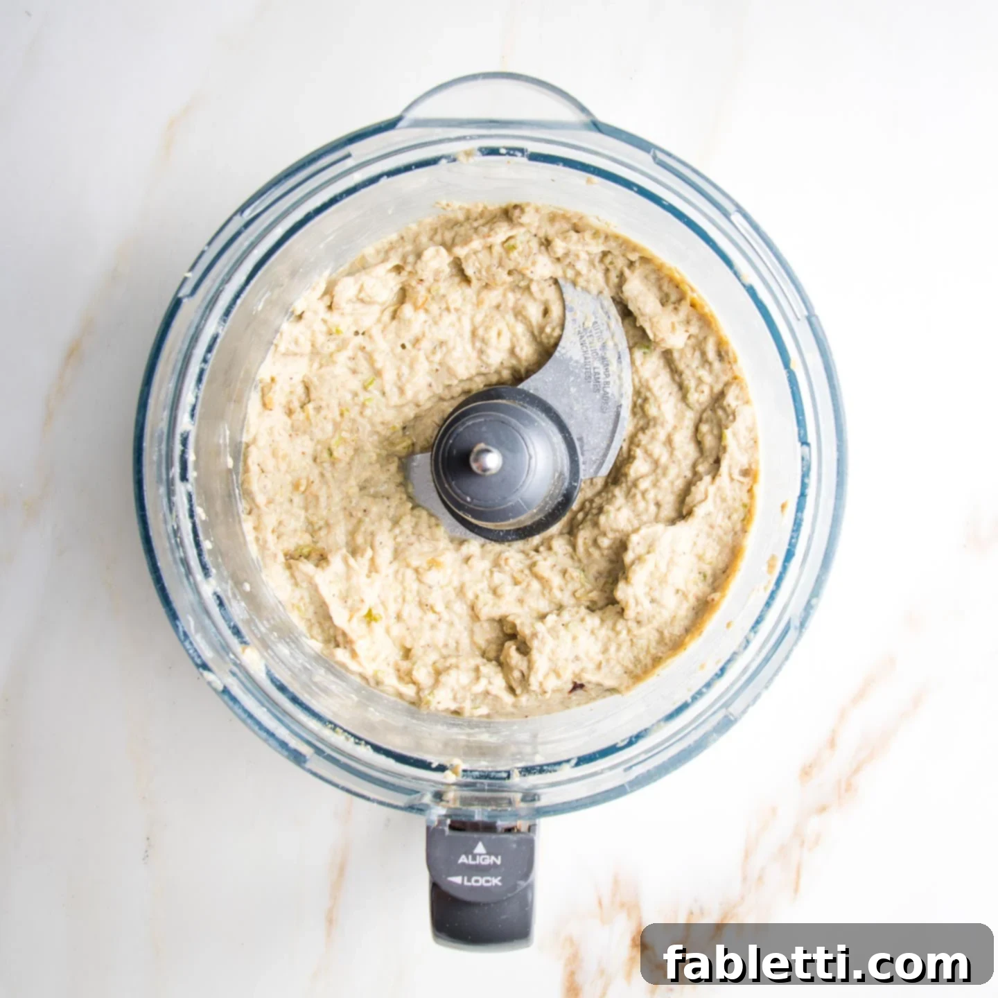 Velvety Roasted Garlic and Tahini Baba Ganoush 11 Beige, creamy dip, with some texture, in the bowl of a food processor.